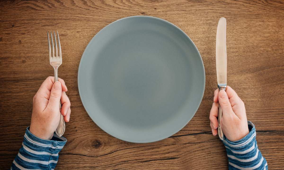 Female hands with fork and knife over empty plate on dining table